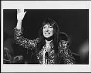 Buffy Sainte-Marie standing in front of a microphone and waving [ca 1995].