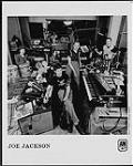 Portrait de presse de Joe Jackson, entouré d'instruments de musique s.d.