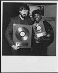 Quality Records remet à Billy Ocean (droite) des disques d'or pour l'album Suddenly et le simple « Caribbean Queen » après le concert à guichets fermés d'Ocean à Toronto. Larry Macrae, directeur de la promotion nationale chez Quality, remet les prix à Ocean [entre 1984-1985].