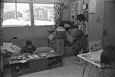 [Kenojuak Ashevak drawing at home as two of her children look on] December 1980