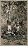 [Anishinaabe woman and child seated outside eating jack-pine inner bark] 1920