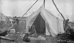Camp scene of a Chipewyan woman seated in front of a tent illustrating the process of pounding moosemeat to make pemmican 1929