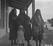 Cree women and a girl standing on a porch. 1926