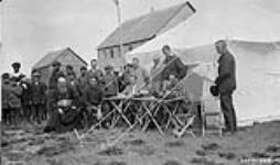 [Group of inidgenous  and non-indigenous men and boys, one in religious garb, sitting in front of tents]. 1928