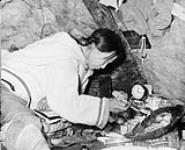 Une femme inuite préparant une lampe alimentée à l'huile de phoque. La photo a été prise lors d'une patrouille de la région est de l'Arctique.  [Arnaujumajuq Piungittuq installant une mèche à sa " qulliq " (lampe à l'huile) dans sa tente.] 1950