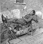 Trooper A.A. Coulombe, 14th Armoured Regiment (The Calgary Regiment), resting on motorcycle. 3 Oct. 1943