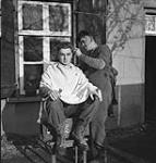 Private Arnold Hintz giving Sergeant Roy Dais a haircut, Mook, Netherlands, 30 November 1944. November 30, 1944.