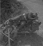 Lance-Corporal Bill Baggott sleeping on his motorcycle, Falaise, France, ca.13-14 August 1944. [ca. August 13 - 14, 1944].