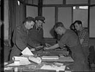 Personnel in composing room of THE MAPLE LEAF. (L-R): Captain Seth Halton, Lieutenant-Colonel R.S. Malone, Sapper Duncan Macnab, M. Charles Niard. 28-Jul-44