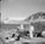 Inuits à l'extérieur de leurs tupiit (tentes); on voit le fjord Pangnirtung et le mont Duval en arrière-plan. [Le nom de l'homme est Evic.]  août 1946.