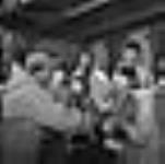 Angmallik distribuant des biscuits aux Inuits qui ont déchargé le ravitaillement de la Compagnie de la Baie d'Hudson du R.M.S. [Les gens qu'on voit sur cette photo pourraient être : Angmarlik, Aipeelee Kilabuk, Akulujuk, Josephie Qaunniq, Pauloosie Angmarlik, Enusiq Nashalik, Attagoyuk, Saki Evic et Archie Angmarlik]. Août 1946