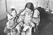 (Mère autochtone coud avec sa fille.)[Niakrok (à gauche) et Kablu (à droite). Kablu est en train de fabriquer des " kamiks " et Niakrok lui joue dans les cheveux.] 1949-1950