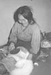 (Femme inuite nettoyant une peau de renard à l'aide d'un ulu. Padlei, T.N.-O., 1949-1950.) [Atatarlik, épouse d'Arnarauyak, faisait le commerce des fourrures de renards avec la Compagnie de la Baie d'Hudson.] 1949-1950