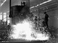 À l'aciérie de Sorel, des ouvriers versent de l'acier en fusion de la poche de coulée dans des moules à lingots. déc. 1940