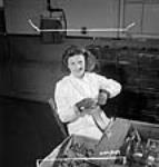Roberte Perry, une ouvrière de l'atelier de munitions à l'usine Dominion Arsenals Ltd, fait fonctionner une machine qui calibre automatiquement les munitions de .303. 24 Aug. 1942