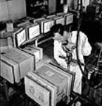 L'ouvrier Raymond Paquette ferme des boîtes d'expédition remplies d'obus avec un tournevis automatique aux usines Cherrier et Bouchard de la société Defense Industries Limited. juil. 1944