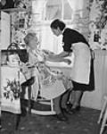 A nurse is tending to an elderly woman's arm during a home visit. c 1945