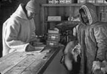 [Atqalluarjuaq (aka Anarusuk), à droite, comptant les jetons offerts pour ses fourrures, lors d'une transaction avec un employé de la CBH, un "qallunaaq" non identifié. Son fils Ubluriaq et sa fille Athithaut vivent encore tous les deux à Arviat.] n.d.