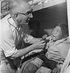 Colatah, deux ans, une petite Inuite de la région du lac Harbour, est examinée à bord du C.D. Howe par le Dr S.H. Campbell de l'équipe médicale en patrouille dans l'Arctique de l'Est [document graphique]. juillet 1951.