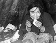 Inuk woman using an ulu (a half round knife) on raw sealskin. 1948