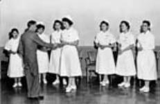 [Presentation of nursing scholarship to Winnifred McKinnon by Mr. P. Deziel - Looking on are other students in various stages of registered nurses training at St. Paul's School of Nursing]. Original title: Presentation of nursing scholarship to Winnifred McKinnon by Mr. P. Deziel - Looking on are other Indian girls in various stages of registered nurses training at St. Paul's School of Nursing  [ca. 1958].