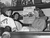 An Inuit boy sitting on top of a counter as Mrs. Sigvaldasson issues Family Allowances to an Inuit woman inside of the Sigvaldasson's store in Cape Smith on Smith Island, Nunavut  1948.