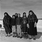 Group of Cree women and children standing in the snow and smiling at the photographer, Chisasibi, Quebec. [Front row: Winnie Matthew-Cookish (second from left), Sarah Ratt (centre), Evie Matthew-House (far right); second row: Elizabeth Matthew (right)]  January 1946.