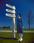 Women's Royal Canadian Naval Service "Wren" summer uniform [Wren standing near signpost indicating HMC shore establishments]. 1943