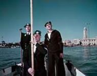 Motor cutter boat crew HMCS MAGNIFICENT  Port Said, serving as part of UNEF (L to R) Mid. J.W. Barlow, Seamen Raymond Dupuis and Stanley Mason. 16-Jan-57