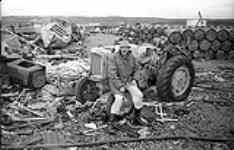 [Mackenzie Porter sitting on a tractor wheel, Iqaluit, Nunavut]. [between 1956-1960]