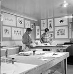 [Iyola Kingwatsiuk (left) and a man examining prints at West Baffin Co-operative, Kinngait, Nunavut]. [between 1956-1960]
