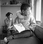 Alma Houston's son sitting with a book indoors, Kinngait, Nunavut]. [between 1956-1960]