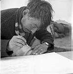 [Artist Kiakshuk drawing inside of a tent, Kinngait, Nunavut]. [between 1956-1960]