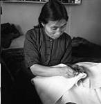 [Nepitia sewing a duffle parka, Kinngait, Nunavut]. [between 1956-1960]