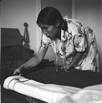 [Nepitia cutting a piece of fabric for a parka, Kinngait, Nunavut]. [between 1956-1960]