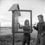 [Two people posting items on a message board]. [between 1956-1960]