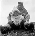 [Paulassie Pootoogook and a boy sitting outdoors, Kinngait, Nunavut]. [between 1956-1960]