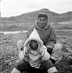 [Paulassie Pootoogook and a boy sitting outdoors, Kinngait, Nunavut]. [between 1956-1960]