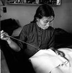 [Nepitia sewing a duffle parka in her home, Kinngait, Nunavut]. [between 1956-1960]