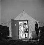 [Mackenzie Porter looking through a bag in a tent at night]. [between 1956-1960]