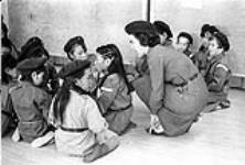 [Brownie group leader Kathy Thompson kneeling beside a group of young girls, Iqaluit, Nunavut]. 1960