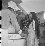 [A man, a woman and Mackenzie Porter (middle) standing around a stove, Iqaluit, Nunavut]. 1960