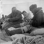 [Mackenzie Porter (left) and a boy watching Kiakshuk (right) create a carving in a tent, Kinngait, Nunavut]. 1960