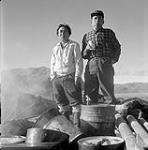 [Spyglassie (left) and Mosesee (right) standing by some oil drums, Iqaluit, Nunavut]. 1960