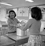 [Two girls holding onto a stock pot in a classroom, Iqaluit, Nunavut]. 1960