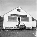 [Barbara Hinds (left) and a boy standing outside the Hudson's Bay Company building, Niaqunngut, Iqaluit, Nunavut]. 1960