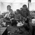 [Kenojuak Ashevak (left), her husband Johnniebo Ashevak (right) and their two children in their tent, Kinngait, Nunavut]. 1960