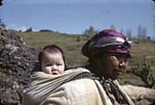 A First Nations woman [Angeline (Brown) Tommy] with an infant [Augustine Morris], standing on riverbank  [1947]