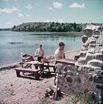Man and woman barbecue at Braemar Lodge on lake Ellenwood, Nova Scotia. 1952