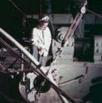 Un homme portant une casquette de capitaine observe des câbles à l'intérieur d'un navire  juillet 1954
